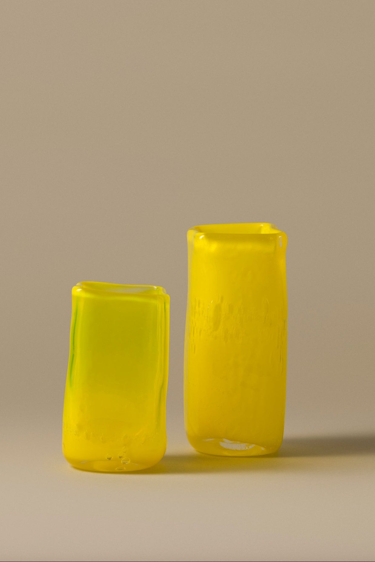 Two yellow glass vases on a beige background